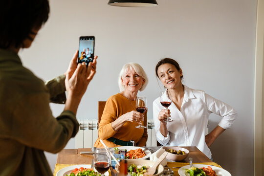 Mature woman taking photo of her friends on cellphone while having lunch