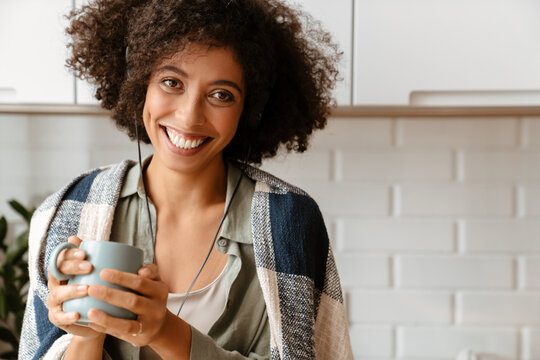 African american woman using earphones while drinking coffee at home
