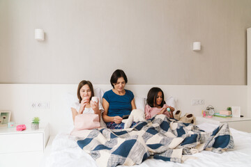 White woman and her daughters spending time together while resting on bed