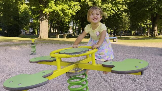 Cute pretty child rides on balancing swing. Little girl laughing and having fun, swinging on seesaw board, playing playground. Concept of happy childhood, positive emotions