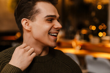 Young white man wearing sweater smiling and looking aside in cafe