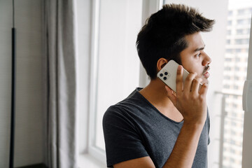 Young handsome indian man talking on phone looking out window