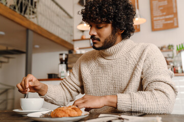Fototapeta na wymiar Young handsome indian curly calm man sitting at cafe