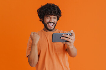 Portrait of young indian curly man holding phone celebrating victory