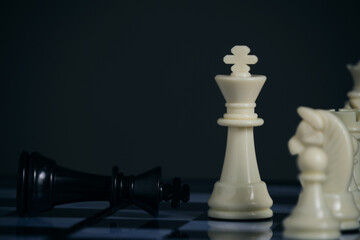 Standing white chess pieces and lying black king.