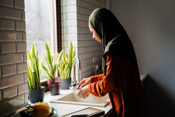 Sideview of young calm woman in hijab washing vegetables