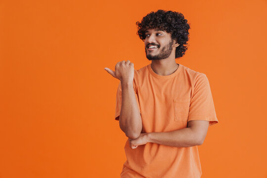 Young indian handsome curly smiling man pointing left with thumb