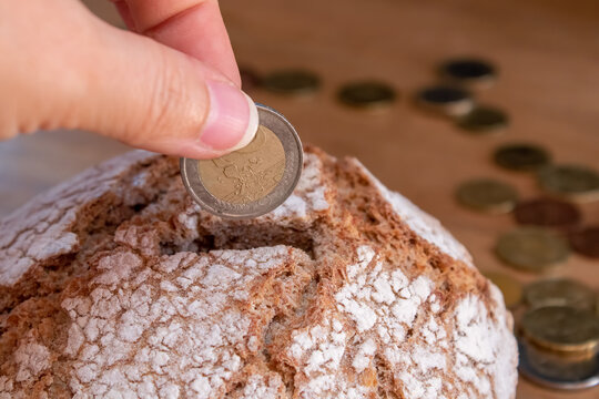 The hand puts the euro coin in the bread like in a money box. Economy, investment in food. food crisis. Agriculture. Agronomy. Bread production. Bakery. Business