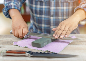 The man sharpen bayonet knife and hiking knife on wooden table.