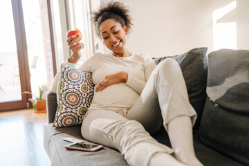 Adult beautiful pregnant smiling african woman eating apple