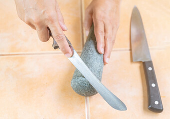 House keeper shapening kitchen knife with pestle stone.