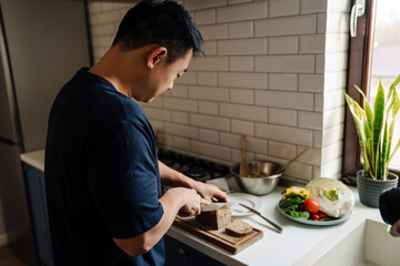 Adult asian man cutting bread on wooden board