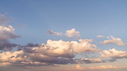 Beautiful panoramic sky replacement sunset background starting at the horizon with layers of fluffy white yellow and pink hued cumulus clouds on a blue sky background.