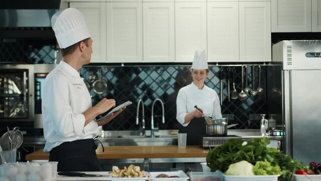 Restaurant kitchen: portrait of male and female cooks. Male Chef checks the availability of products in the warehouse using a tablet