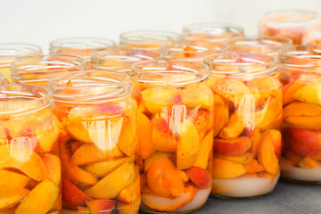 Apricot slices with water and sugar in jars. Homemade fruit compotes ready to be lidded and sterilised. Preparing winter supplies at home