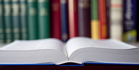A big open book on the table before a bookshelf at the background. The concept of learning, research, education and back to school experience.