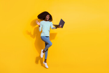 Full length photo of overjoyed astonished girl jump stare wireless netbook isolated on yellow color background