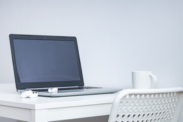 Fototapeta na wymiar Laptop, cup, wireless headphones on a white table, white chair. Workplace.