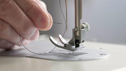 Preparation for sewing. Seamstress inserts thread in needle of sewing machine, side view. Tailor is working in workshop. Sewing workshop. Concept of Factory, Home, At Work, Professionals