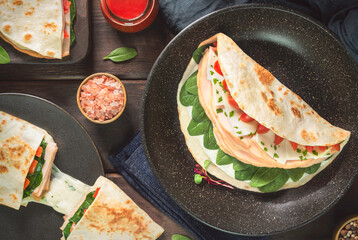 Fresh healthy turkey tortilla wraps with egg whites, baby spinach, mozzarella slices and cherry tomato. Served with sriracha sauce. Top view with close up.