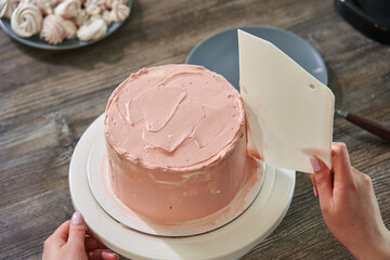 a woman's hand with a large spatula smoothes pink cream on a round cake