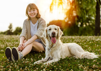 Portrait of teenage girl petting golden retriever outside in sunset