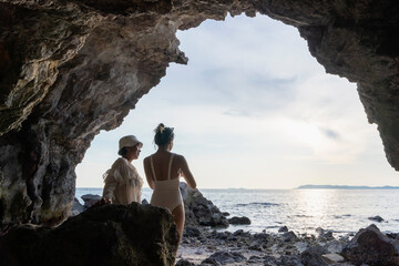 Two women taking photos in cave overlooking sea at sunset or sunrise. Mother and daughter relaxing...