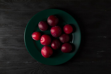 Plums on the green plate and black wood background.