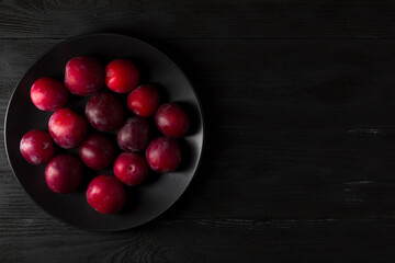 Plums on the black plate and black wood background.