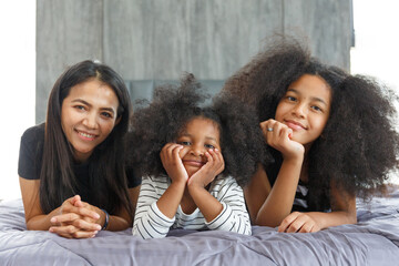 Portrait Asian mother with mixed ethnic daughter two cute little girls lounging in bed in the bedroom at home