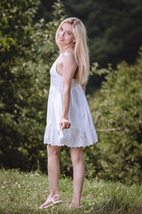 Fototapeta premium young blond woman in a white dress posing in nature and smiling