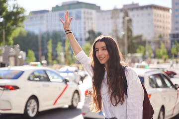 Young woman hailing a taxi on city street. Concept of transport, travel and tourism - obrazy, fototapety, plakaty