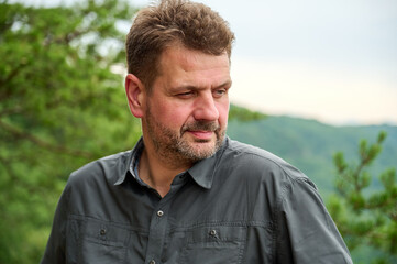 a middle-aged man of 45 year old is looking thoughtfully sideways on a cloudy day with pine tree branches in the background 