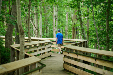 Fayetteville, West Virginia, USA - June 26th 2022: a man dressed in shorts and a t-shirt is fast walking along the wooden bridge after enjoying the view of New River Gorge Bridge on an overcast day.Fa