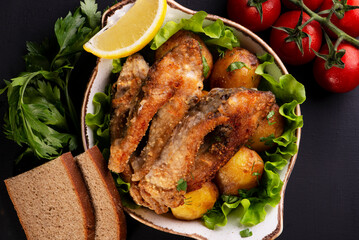 fried fish and baked potatoes on a dark background