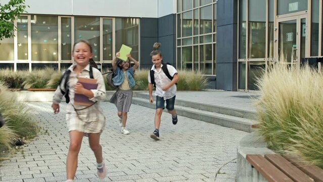 Group of elementary school students joyfully run out of the school building. End of lessons.