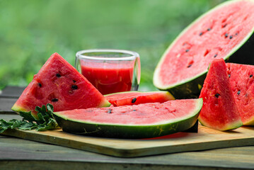 Delicious watermelon  outdoors wooden  table, GREEN  natural background sunny day, Heap,  Fresh ripe red, leaf, summer sunny garden juice drink organic sweet fruit, vegan food Tasty sliced board plate