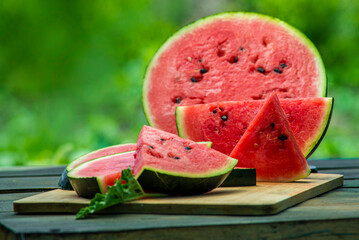 Delicious watermelon  outdoors wooden  table, GREEN  natural background sunny day, Heap,  Fresh ripe red, leaf, summer sunny garden juice drink organic sweet fruit, vegan food Tasty sliced board plate