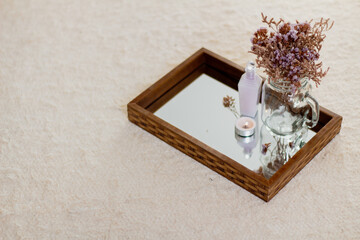 Dried flowers vase, soap, skin care products and candle on mirror tray. Aesthetic minimalist composition.