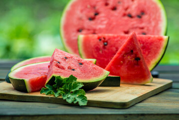 Delicious watermelon  outdoors wooden  table, GREEN  natural background sunny day, Heap,  Fresh ripe red, leaf, summer sunny garden juice drink organic sweet fruit, vegan food Tasty sliced board plate