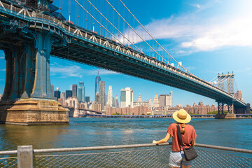 Young woman enjoying view of city skyline in New York. Happy lifestyle girl with hat traveling tourist on bridges.