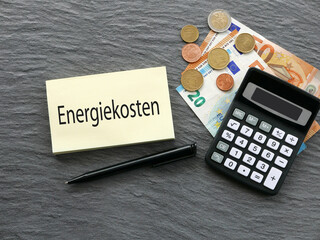 Das Wort Energiekosten auf einem Notizblock  mit Euro Banknoten und Taschenrechner.