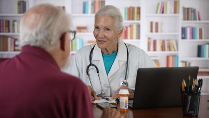 Mature senior female doctor talking to male patient in modern clinic with library background.