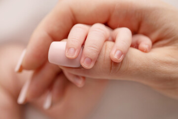 Obraz na płótnie Canvas Close-up of a baby's small hand with tiny fingers and arm of mother on a white background. Newborn baby holding the finger of parents after birth The bond between mother and child Happy family concept