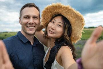 Mixed race couple of millennial in a grass field taking a selfie with a smartphone.