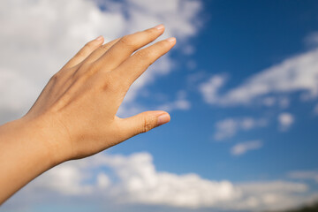 Female hand palm on the blue sky with clouds