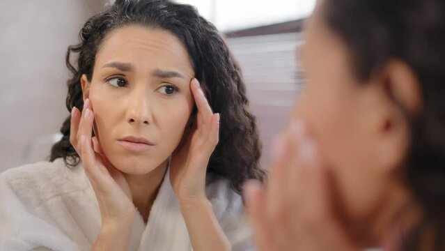 Headshot upset worried sad woman looking at mirror dissatisfied with condition of skin after new cosmetic substandard product frustrated girl worrying about first wrinkles in eye area and facial skin