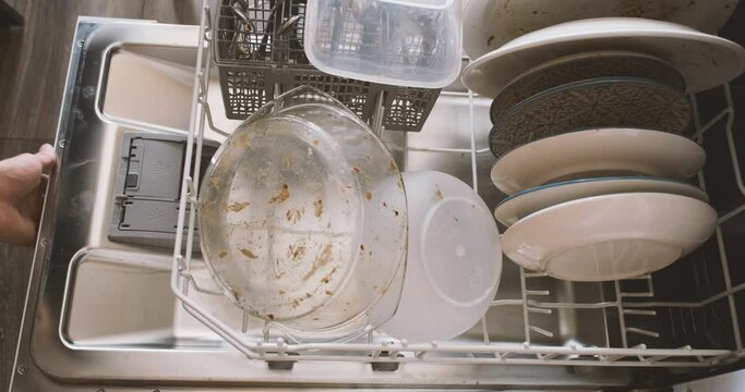 Man's hand loads tray with dirty dishes into the dishwasher and closes the lid. Top view, close-up. The concept of homework, washing dishes, home life.