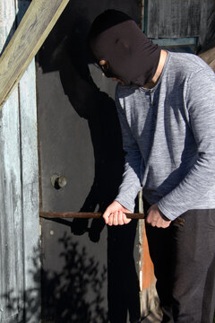 a thief in a black mask breaks down the door with a crowbar