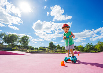 Boy on the kick scooter ride around orange cones at skate park © Sergey Novikov